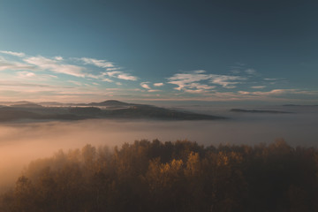 Aerial view to autumn trees with misty fog and hill in sunrise, Czech landscape, toned photo