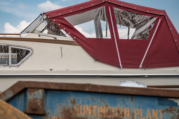 Abstract of a large cabin cruiser located at a boat yard, seen behind a large industrial skip. The...