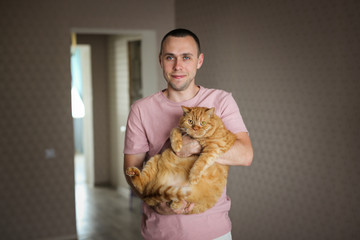A man with a very fat red cat in his arms, pets