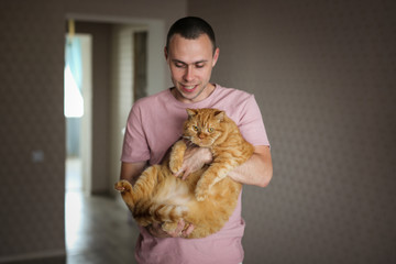 A man with a very fat red cat in his arms, pets
