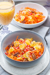Healthy raw vegetarian salad with carrot, pomegranate seeds, oranges, pumpkin seeds, pecan nuts in grey bowl. Glass of orange juice and pomegranate on the background.