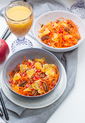 Healthy raw vegetarian salad with carrot, pomegranate seeds, oranges, pumpkin seeds, pecan nuts in grey bowl. Glass of orange juice and pomegranate on the background.