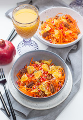 Healthy raw vegetarian salad with carrot, pomegranate seeds, oranges, pumpkin seeds, pecan nuts in grey bowl. Glass of orange juice and pomegranate on the background.
