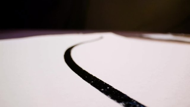 Pan shot of a calligraphy paintbrush leaving marks of black ink on white paper