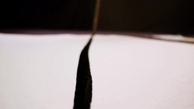 Pan shot of a calligraphy paintbrush leaving marks of black ink on white paper