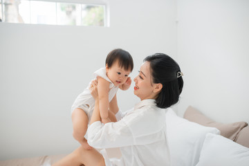 Fototapeta premium Young mother playing with her baby in bedroom at home