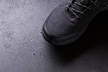 Black men's sneakers with drops of water, close-up on a black isolated background.