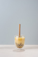 Bubble boba tea with milk and tapioca pearls in glass on blue background