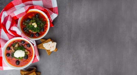 Ukrainian and Russian cuisine. Red borsch on a grey background. Red textile towel. Borsch with vegetables and tomato dill, black olives, lard, bread slices