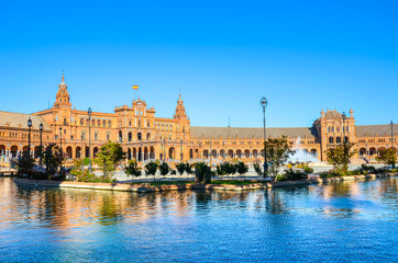 Amazing Plaza de Espana in Seville, Spain. Water reflection of the palace buildings on the adjacent canal. One of major Spanish tourist attractions. Regionalism architecture. Sevilla, Andalusia - obrazy, fototapety, plakaty