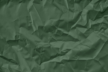 Trendy dark green colored textured background. Crumpled satin paper texture. Flat lay.