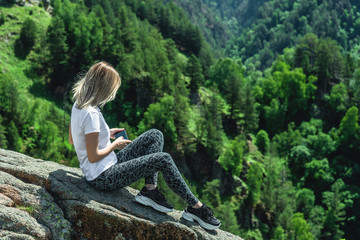 Naklejka na ściany i meble A woman sits high in the mountains, among the greenery, relaxing on vacation.