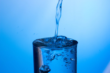 Chorro de agua cayendo sobre un vaso lleno de agua, saltando gotas y chapoteo