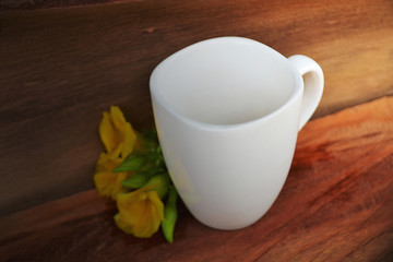 White coffee cup Placed on old wooden floors and natural backgrounds with yellow flowers.