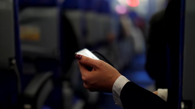 Woman watch movie using phone during flight, lean to aisle of airliner. Camera show passenger face then pan down to mobile device and back up, blurred background. Economy class cabin of Asian airline