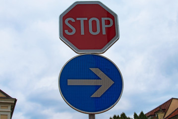 Two road signs. Traffic sign stop and blue road sign with white arrow to the right against cloudy sky. Concept of road sign in city. Maribor, Slovenia