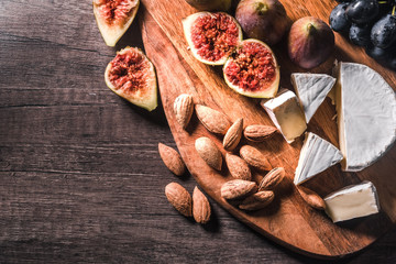 Cheese plate served with grapes, figs and nuts on a wooden background.