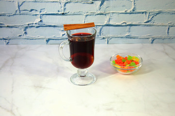 A glass of mulled wine with an orange and a stick of cinnamon, next to a plate of dried fruit.