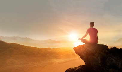 Woman practices yoga and meditating on the mountain sunset background.