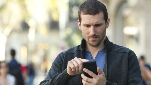 Front view of a serious adult man checking smart phone standing in the street