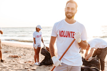 Smiling young confident man volunteer cleaning beach