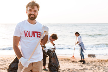 Image of enthusiastic young volunteers cleaning beach from plastic