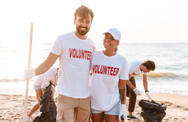 Image of smiling young volunteers cleaning beach from plastic