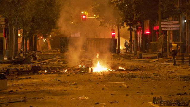Fire from a protest riot burns in the street, while tear gas guns and emergency sirens are heard in the distance amid protest in Barcelona, Spain in October 2019. ProRes file, shot in 4K UHD.
