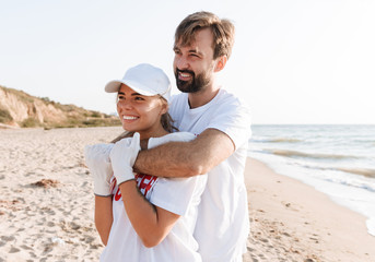 Image of romantic nice couple hugging while cleaning beach