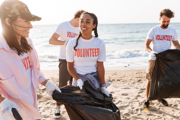 Image of happy eco volunteers cleaning beach from plastic