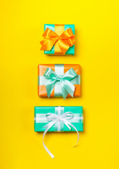 Stack of attractive gifts on the yellow background. Trendy orange and green colors. Merry Christmas, St. Valentine's Day, Happy Birthday and other holidays concept. Copy space. Flat lay