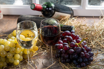 Glasses of red and white wine with grape, bottles at background