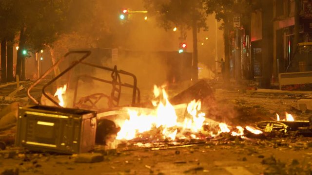 Fire from a protest riot burns in the street, while tear gas guns and emergency sirens are heard in the distance amid protest in Barcelona, Spain in October 2019. ProRes file, shot in 4K UHD.