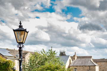 Wrought iron lampost seen against a summer's sky in a North Yorks market town. Distance, stone built houses can be seen in the distance.