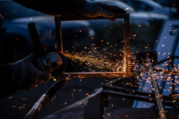Fototapeta na wymiar Sparks from metal sawing. A man is cutting a metal profile with a grinder. Work in the garage. Creation of construction. Sparks from heating. The disc rotates and cuts metal.