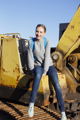 Fototapeta na wymiar Young happy woman sitting on an yellow excavator.