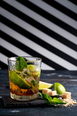 Whiskey and Cola cocktail with lime, mint, brown sugar and ice, alcoholic drink in a glass on a dark wooden background, copy space