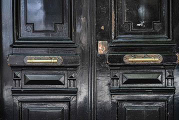 Old wooden door. Black painted wooden door glossy surface closeup. Aged wood panels with shiny brass vintage doorknobs and lock patch. Architectural details of Paris door of old building in France.