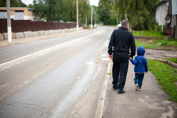 A man walks with a child along the street along the road. Kick the child by the hand when moving near the roadway.