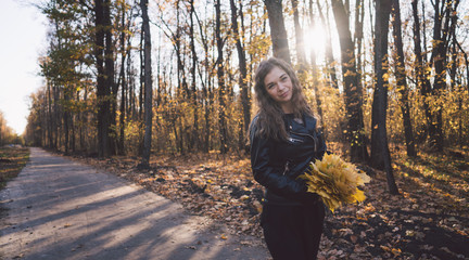 Beautiful woman posing standing in autumn forest. Girl in leather black jacket walking in the forest