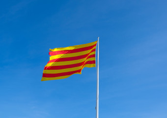 Flag of Catalonia. Senyera, vexillological symbol. Red and yellow strips flag isolated on clean blue sky background. Flag waving in the wind in sunny day, symbol of freedom. Catalonia, Spain. 