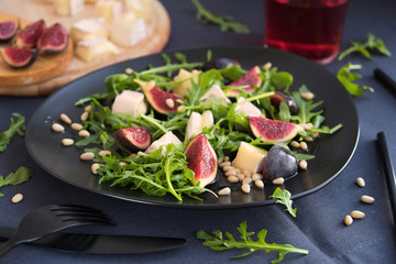 CAMEMBERT AND FIG SALAD on black plate in dark grey tablecloth.