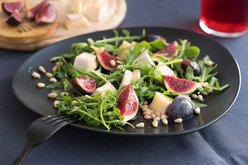 CAMEMBERT AND FIG SALAD on black plate in dark grey tablecloth.