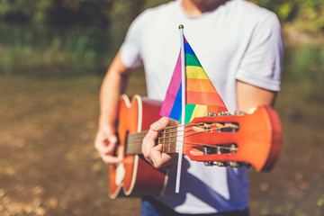 Gay guitar player holding acoustic guitar with pride flag outdoors. Space for copy.
