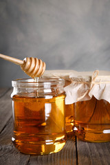 Pouring aromatic honey into jar, closeup. Honey in glass jars and honeycombs wax on wooden background. Wooden stick , instruments