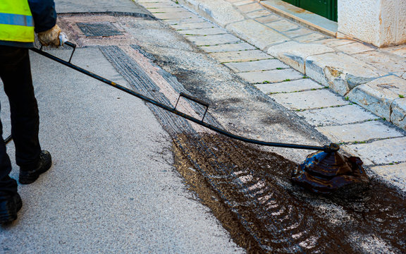 Partial repair of the asphalt road. The worker sprays bitumen on the asphalt surface. The road maintenance worker sprays the bitumen mixture onto the cleaned