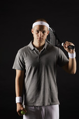 Portrait of young man holding racket and looking at camera over black background