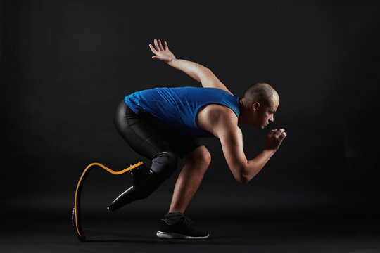 Side view of paralympic sportsman in sports clothing and with prosthesis instead of leg running over black background