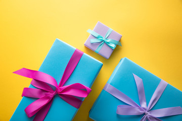 top view of colorful gift boxes with ribbons on yellow background