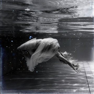 Black and white image. Underwater photo beautiful blonde wearing in white flying dress, swimming in pool underwater.